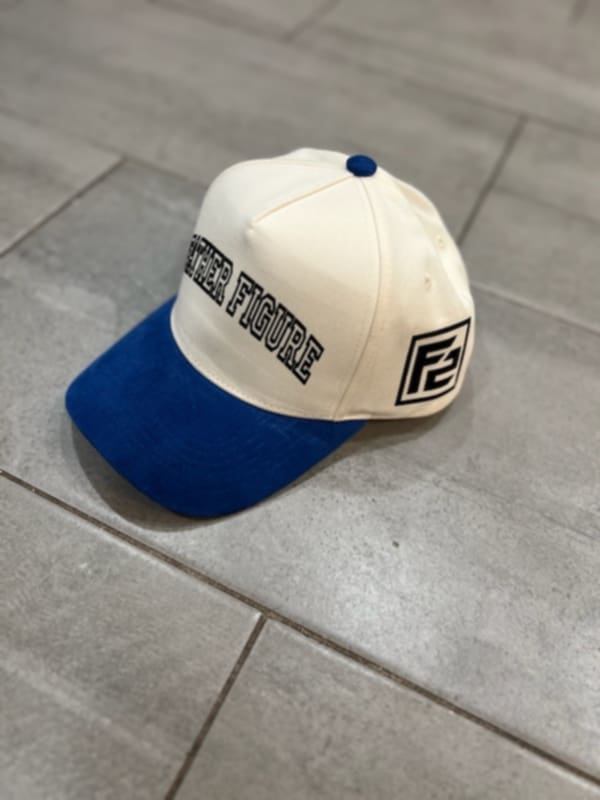 A cream-colored baseball cap with blue corduroy brims and text that reads 'Father Figure' on the front.